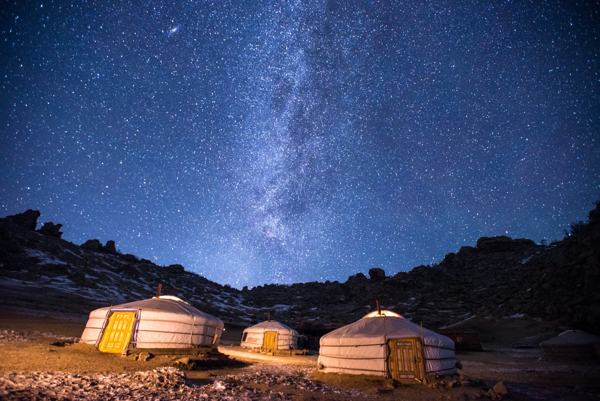 Three lit yurts on a stony plain beneath the Milky Way