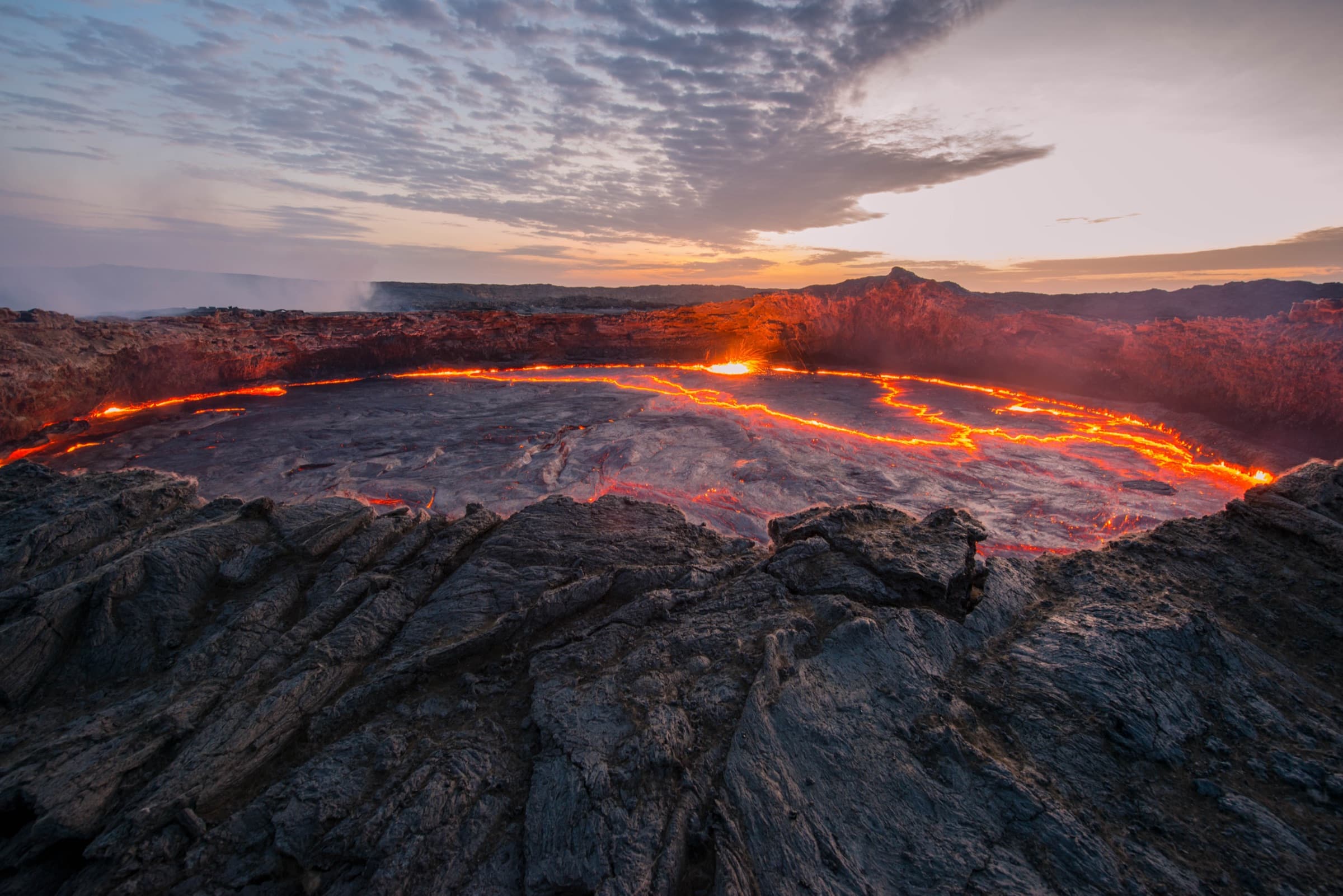 A lava lake glowing orange inside a volcanic crater at dusk