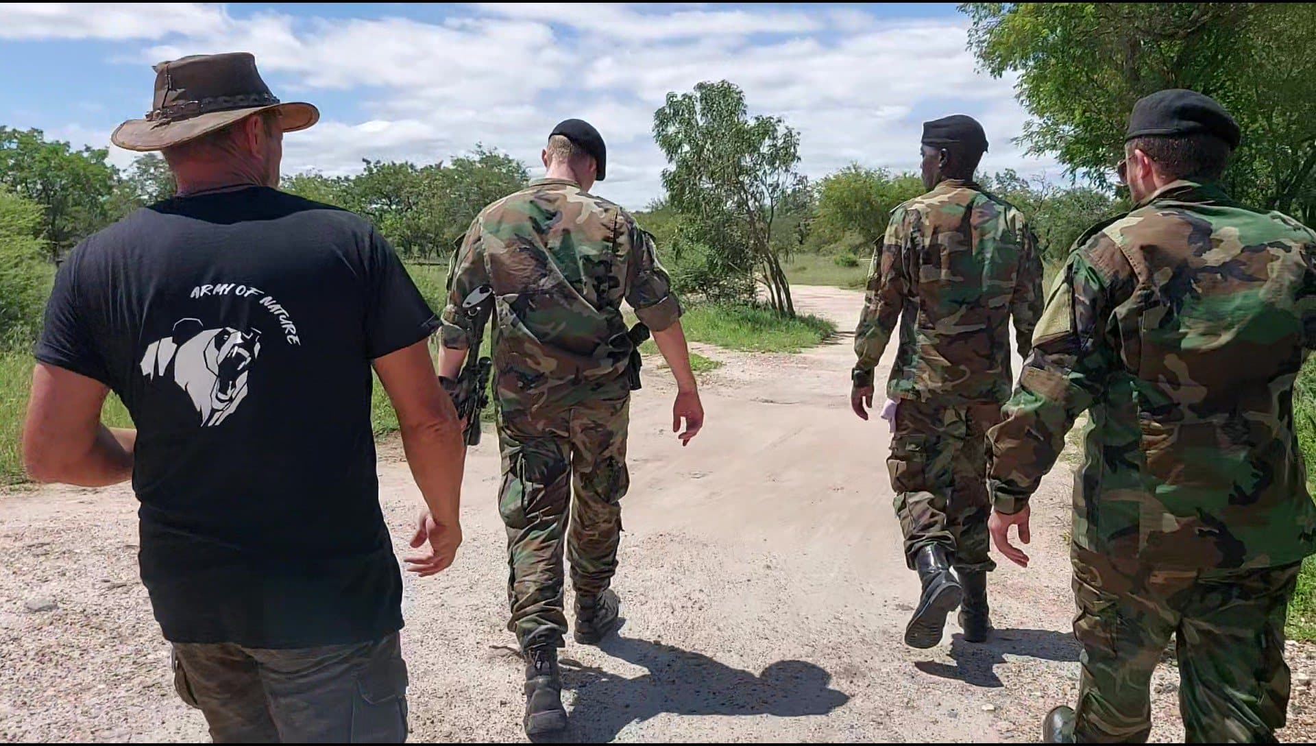 Four people walking away down a bush road, the nearest in an Army of Nature T-shirt, three in camouflage