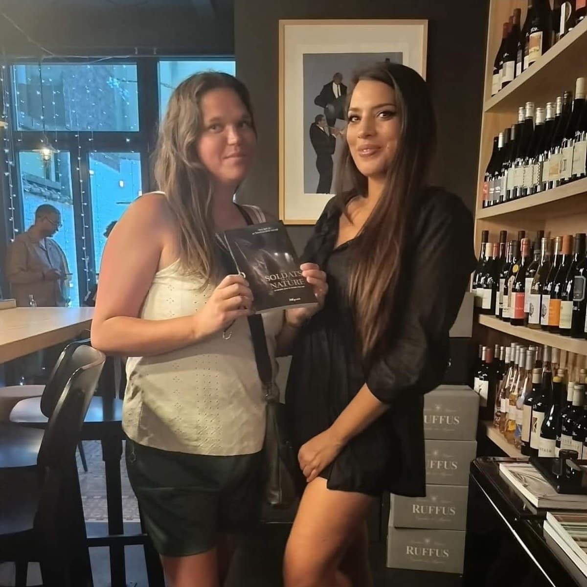 Two readers in a wine bar holding up a copy of Les Soldats de la Nature